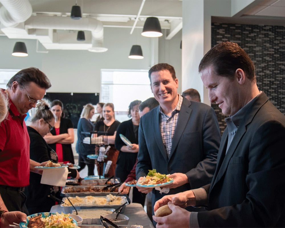 Coworkers fill their plates at a buffet line in the office.