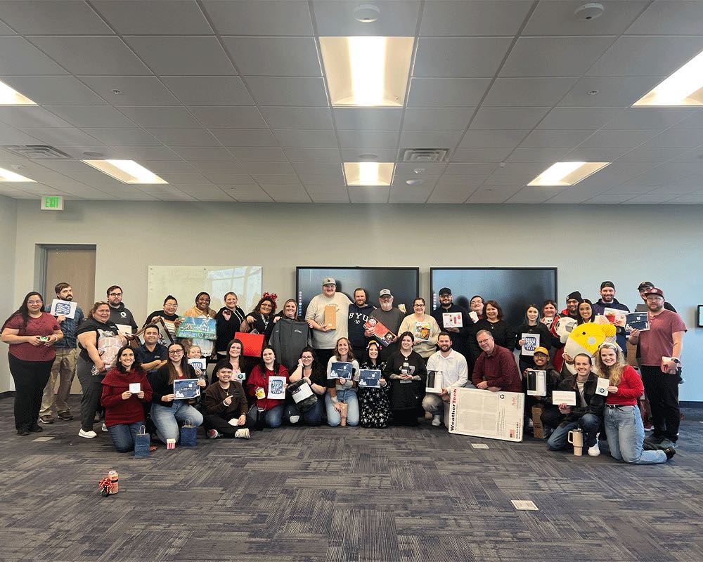 A large team group photo in an open office, many holding certificates and cards.