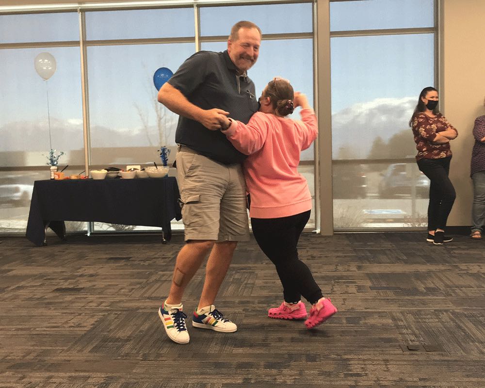 Two coworkers dance together at an office party with balloons.