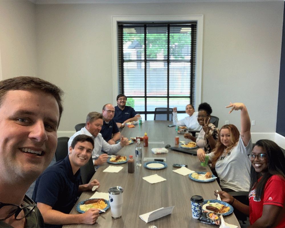 A selfie of a team eating lunch together at a long conference table.
