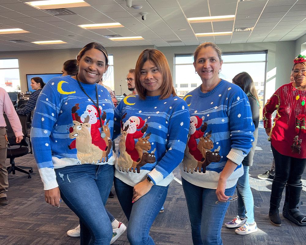 Three coworkers pose in matching blue holiday sweaters.