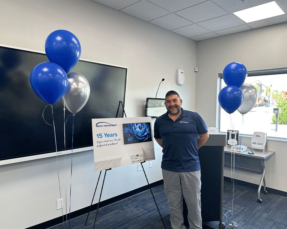 A team member stands beside a 15 Years anniversary sign and blue balloons.