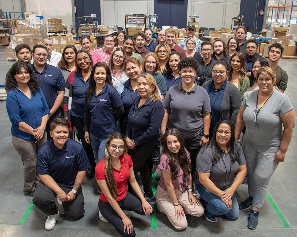A large team group photo in the warehouse, most in navy AE shirts.