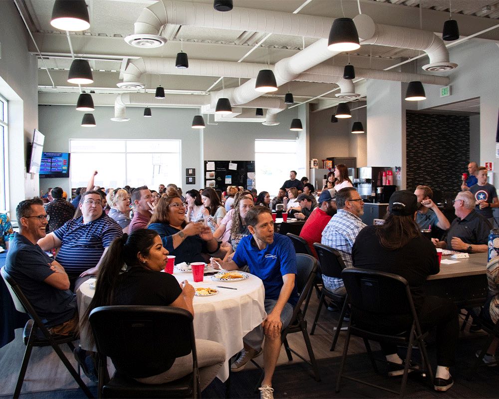 A full room of coworkers seated at round tables for a company lunch.