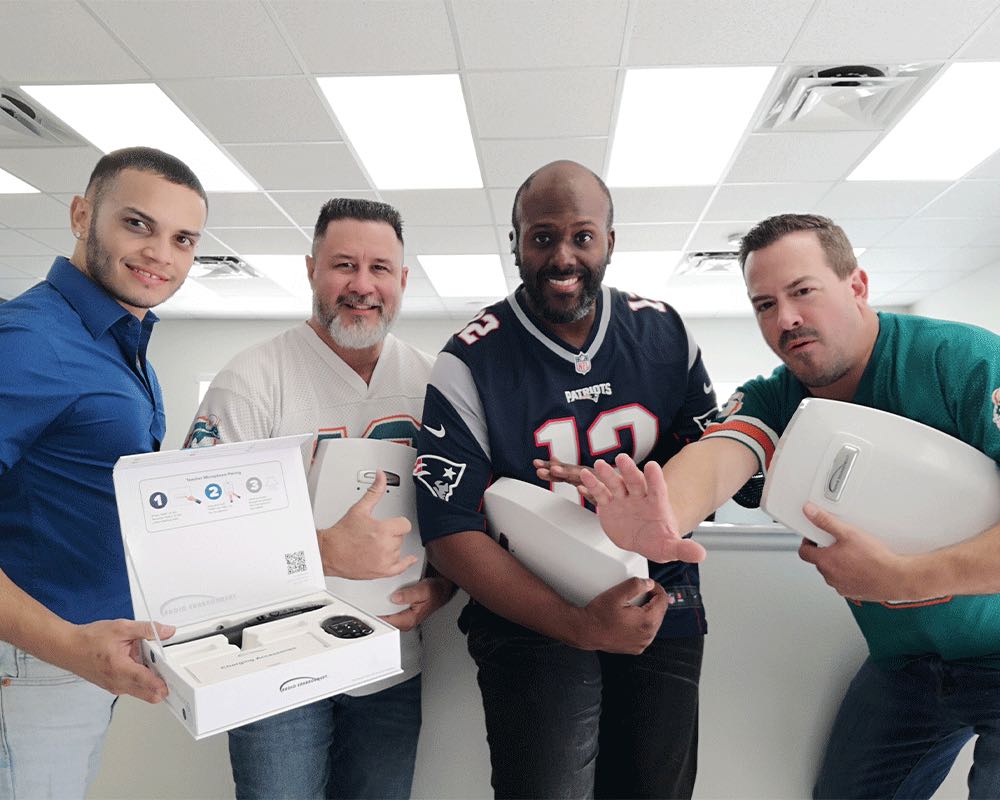 Four coworkers in football jerseys hold classroom speakers and a boxed microphone.