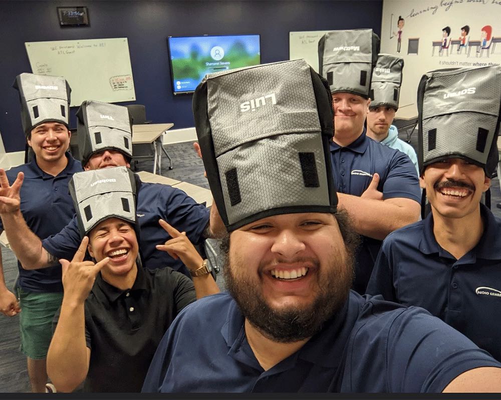A group selfie of coworkers wearing speaker carrying bags as hats.