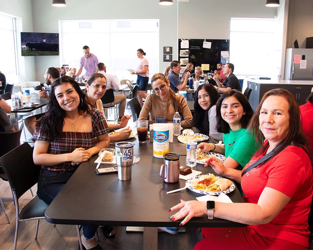 Coworkers smile across a lunch table in the break room.