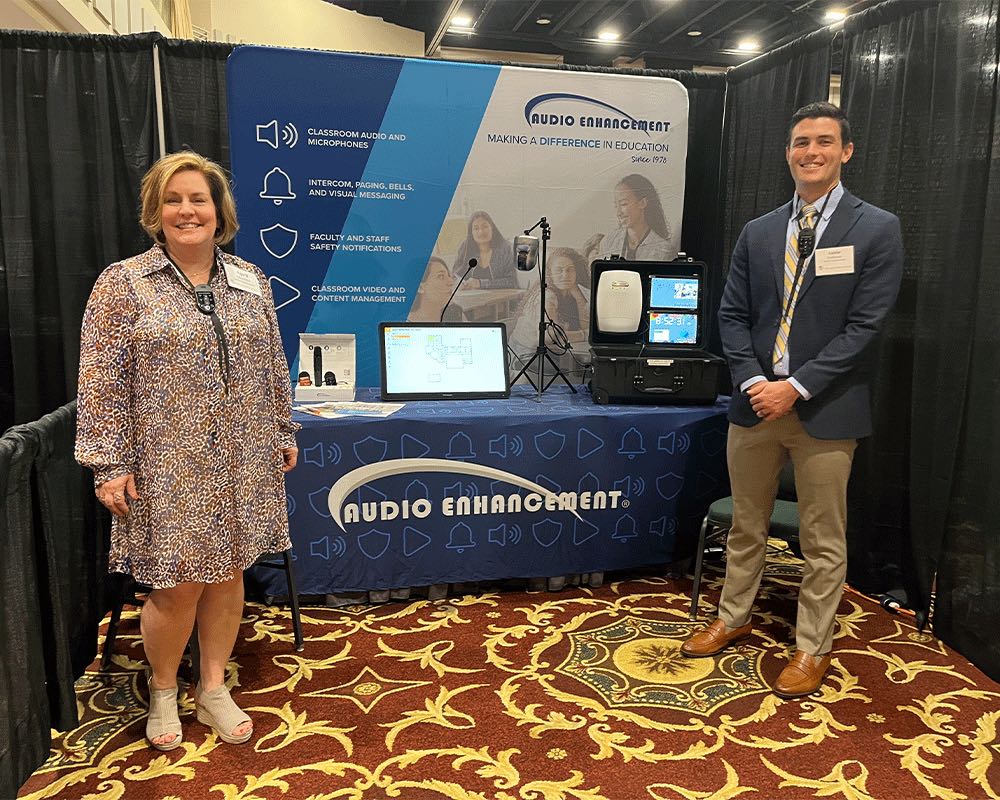 Two team members at an Audio Enhancement trade show booth.