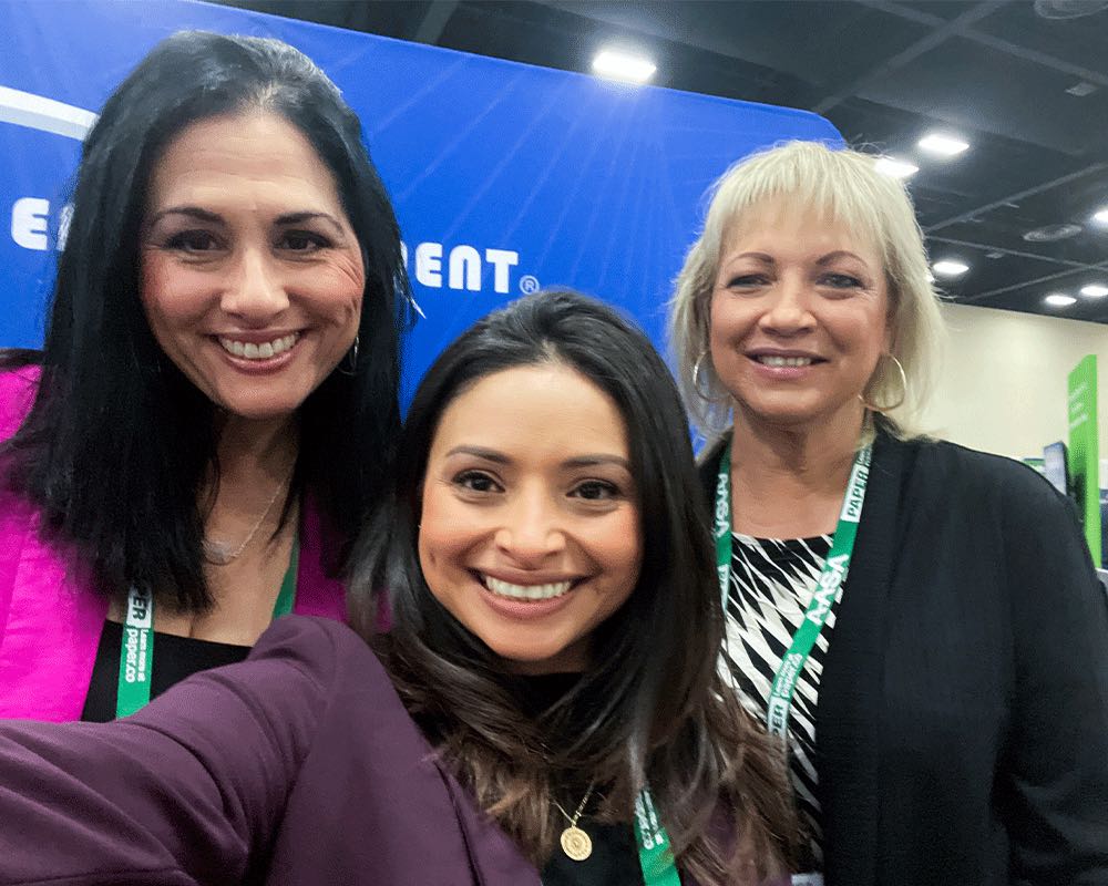A selfie of three coworkers with lanyards at a conference.